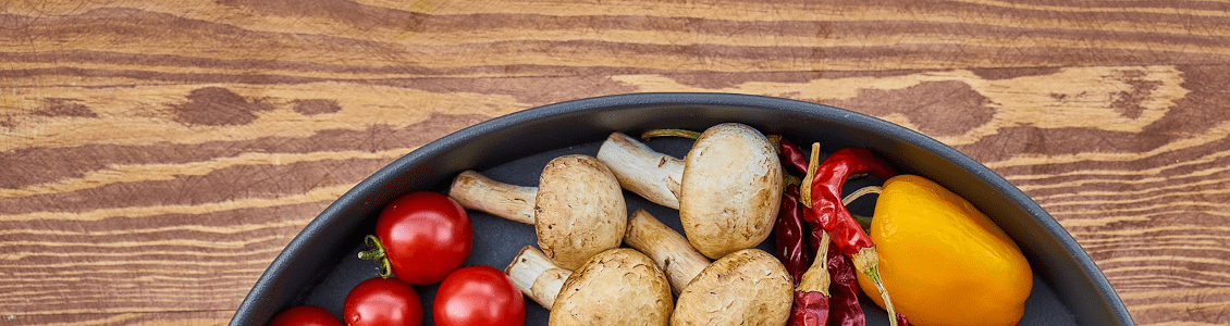 Cherry tomatoes, chestnut mushrooms, chillies and yellow peppers laid out in a pan on a wooden table