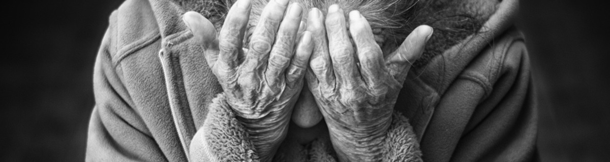 An older person sitting with their head in their hands, looking overwhelmed