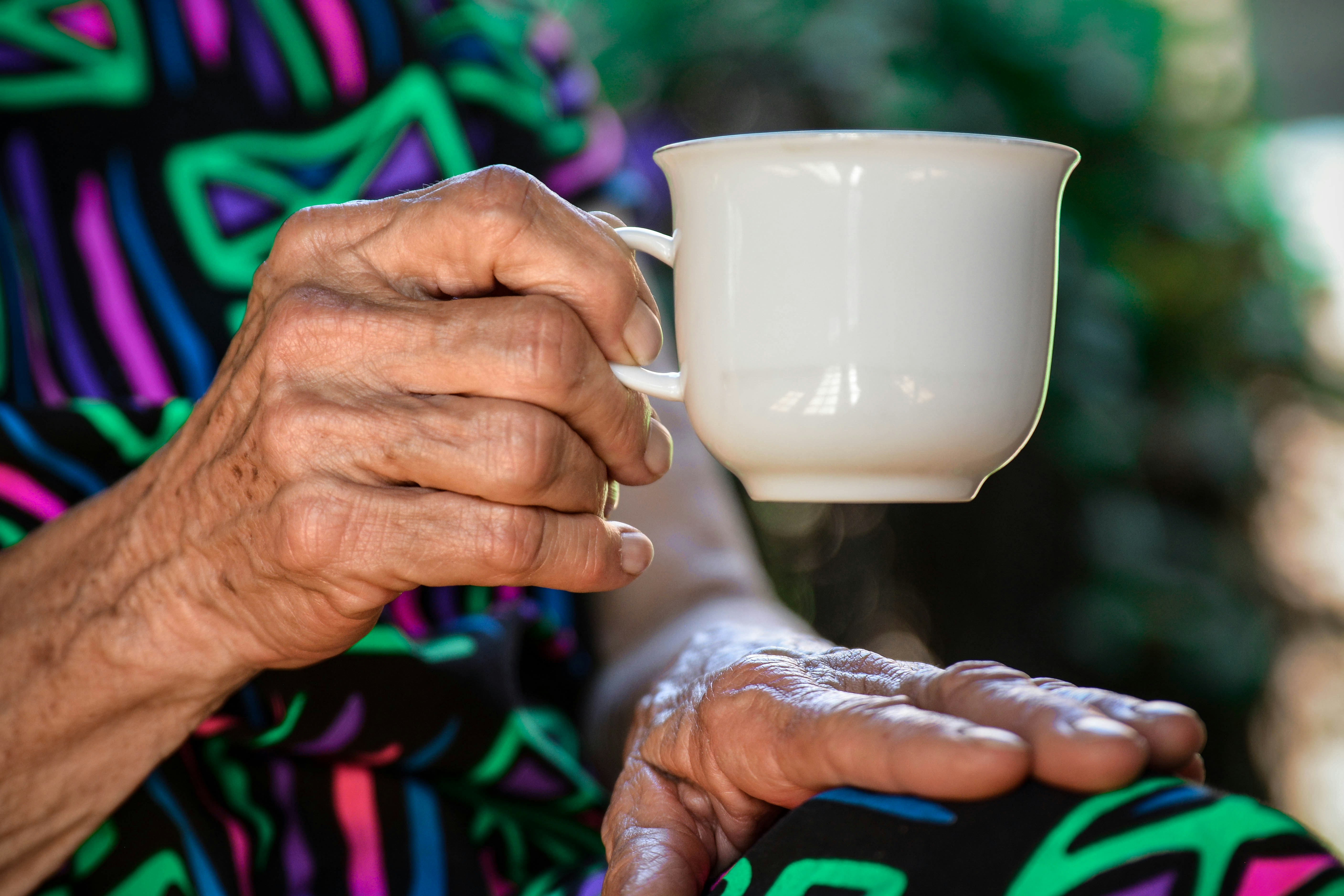 Close-up of an older person's hand holding a white cup of tea