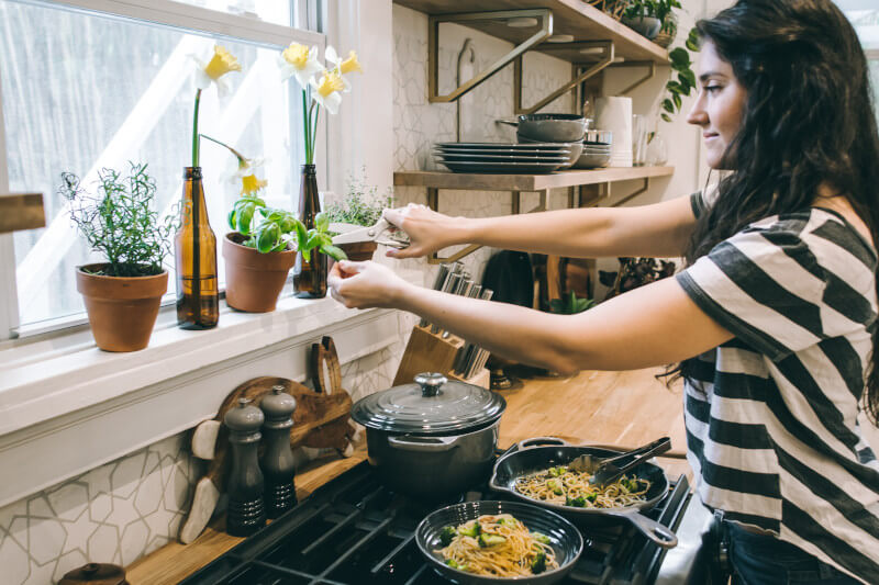 A woman cooking a pasta dish with fresh herbs in a home kitchen