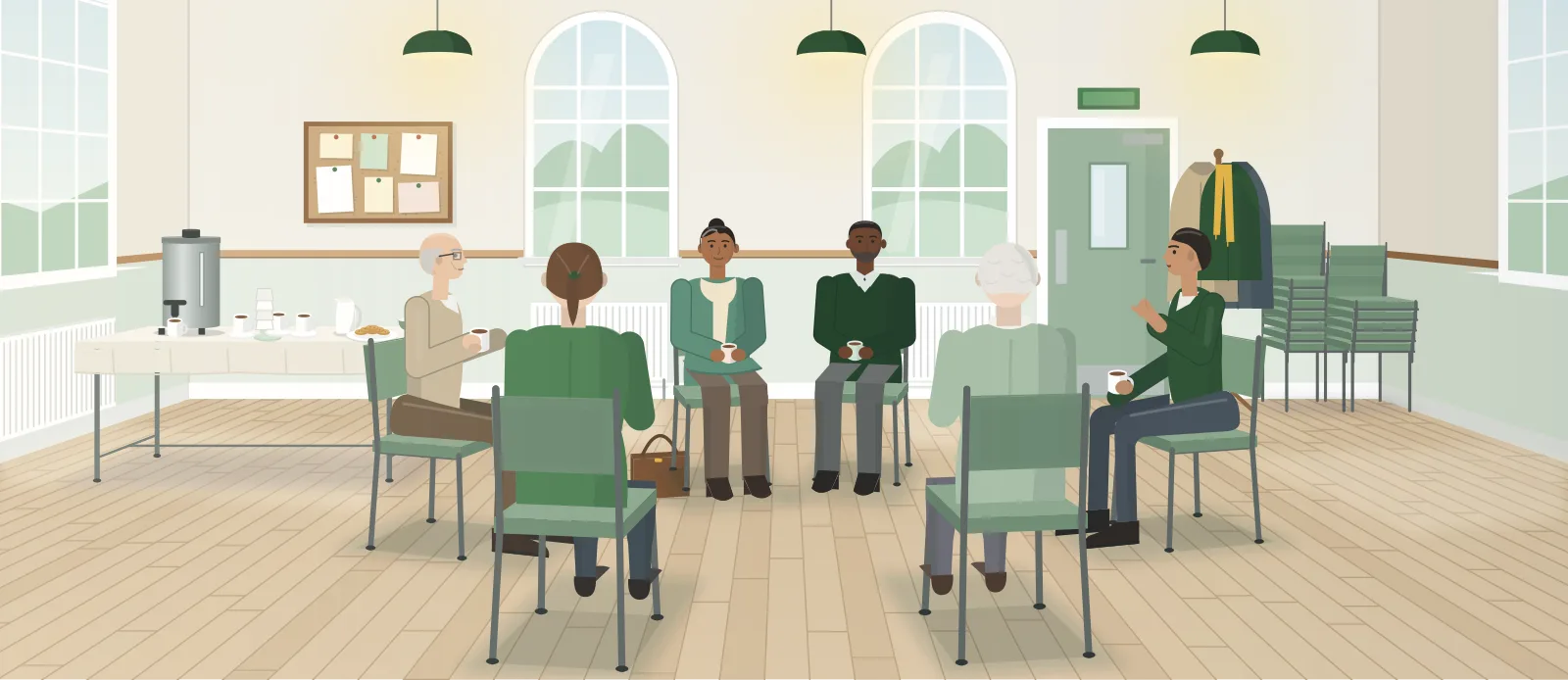 Six people sitting in a circle of chairs in a bright community hall, holding cups of tea and listening to one woman speak, with an urn and cups on a table by the wall